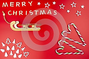 The Inscription Merry Christmas made of wooden letters, lying flat from above, isolated on a red background. Visible candy canes,