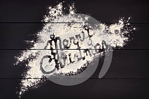 The inscription Merry Christmas , written with flour on a dark wooden background. Christmas greeting card.