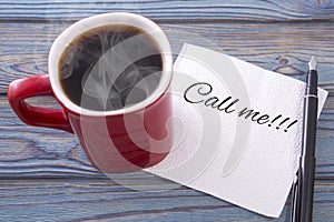 Inscription on a napkin Call me. and coffee in a red cup. Against a background of blue wood