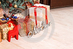 The inscription `New Year` and boxes with gifts near a green New Year`s fir-tree, and together with them the red horse