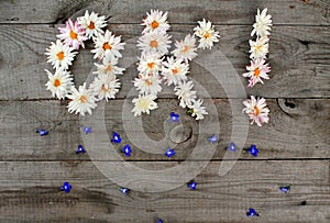Inscription `OK!` from flowers on wooden background with scattered flowers and copy space.