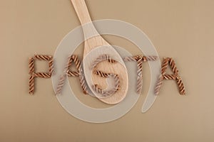 Inscription PASTA lined of uncooked fusilli. Wooden spoon. Design element. Gluten free flax pasta. Uncooked Fusilli made of
