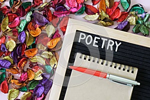 The inscription poetry next to a notebook, a fountain pen and a lot of multi-colored dry leaves and petals. The concept of poetic