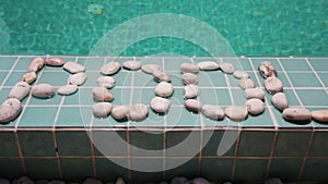 The inscription `pool` is laid out by pebble on a pool side