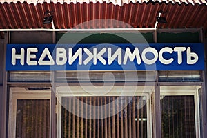 The inscription Real estate in Russian above the entrance to the agency of realtors. Translation