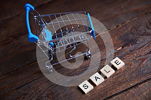 The inscription Sale and shopping cart on a wooden background.