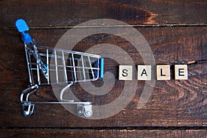 The inscription Sale and shopping cart on a wooden background.