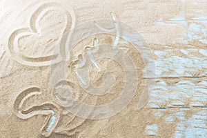 Inscription on a sandy beach on a light wooden background.