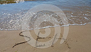 The inscription sea on the sand by the water and the rising wave, seashore beach vacation by the sea