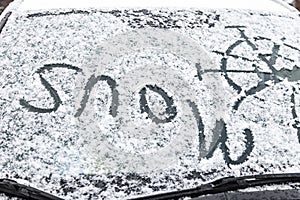 The inscription snow, on the front windshield of the car, covered with snow