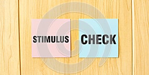 Inscription STIMULUS CHECK on pink and blue square sticky sticker on wooden wall