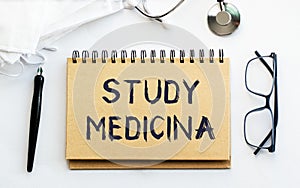 Inscription - STUDY MEDICINA. Written in a notepad to remind you of what`s important. Top view of the table along with a photo