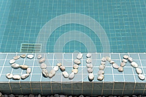 The inscription `swim` is laid out by pebble on a pool side