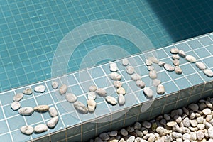 The inscription `swim` is laid out by pebble on a pool side