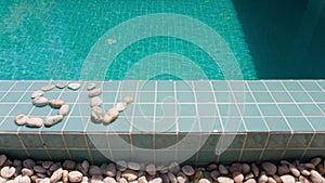 The inscription ` swim ` is laid out by pebble on a pool side,stop-motion