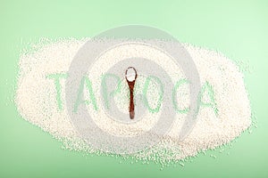 Inscription Tapioca of tapioca pearls on green background. White small sago balls in wooden spoon. Top view, design element