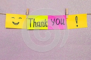 The inscription thank you on colored paper, attached with clothespins to a rope on a pink background