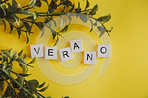 The inscription verano in spanish on the letters of the keyboard on a yellow background with branches of flowers photo