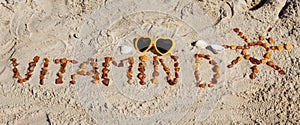 Inscription vitamin D with shape of sun and sunglasses on sand at beach. Prevention of vitamin D deficiency