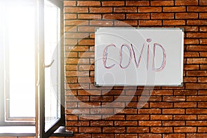 The inscription on the wall is the word COVID. Brick brown wall in a room with a window