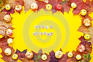 Inscription of wooden blocks hello autumn. Frame made from red and orange autumn maple leaves and garden apples on a