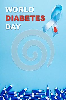 Inscription world diabetes day and blue ribbon awareness with red blood drop and line of lancets on a blue background
