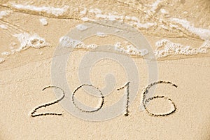 2016 inscription written in the wet yellow beach sand being wash