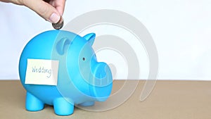 Insert coins in blue piggy bank with sticky note and wedding word on concept of saving money for wedding