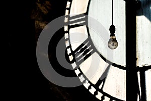 Inside abandoned old ancient clock tower with Roman numerals gears and close up of light bulb hanging down with feathers