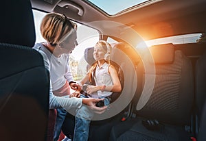 Inside the car photo of a mother fastening with safety auto belt her little daughter girl sitting in child seat. Girl listening