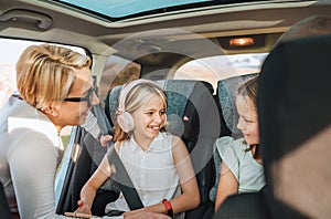 Inside the car photo of a mother fastening with safety auto belt her little daughter girl sitting in child seat. Girl listening