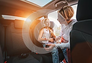 Inside the car photo of a mother fastening with safety auto belt her little daughter girl sitting in child seat. Girl listening