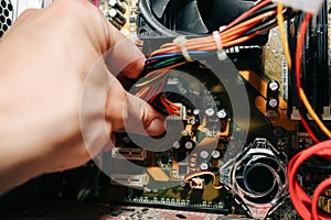 Inside details of the old personal computer. Cooler, motherboard, wires and video card in the dust. Man is holding cables in his