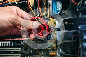 Inside details of the old personal computer. Cooler, motherboard, wires and video card in the dust. Man is holding cables in his