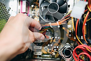 Inside details of the old personal computer. Cooler, motherboard, wires and video card in the dust. Man is holding cables in his