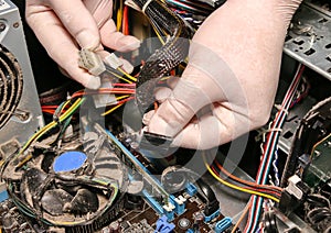 Inside details of the old personal computer. Cooler, motherboard, wires and video card in the dust. Man is holding cables in his