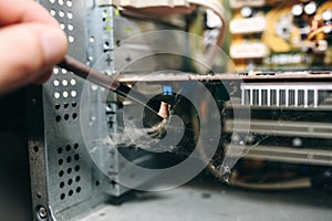 Inside details of the old personal computer. Motherboard and video card in the dust. Man is cleaning wires with a brush. Broken PC