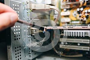 Inside details of the old personal computer. Motherboard and video card in the dust. Man is cleaning wires with a brush. Broken PC