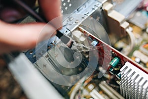 Inside details of the old personal computer. Wires and video card in the dust. Man is cleaning motherboard with a brush. Broken PC