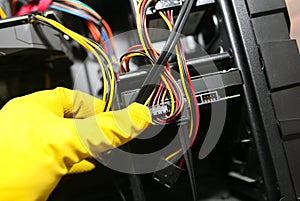 Inside details of the personal computer. Man is cleaning wires in yellow gloves. Motherboard and video card in the dust. Broken PC