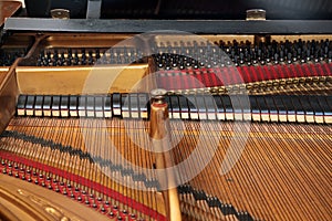 Inside a grand piano with metal frame, strings, hammer and damper, view into the mechanics of an older acoustic musical instrument