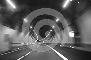 Inside a highway tunnel a car turning left in black and white blur effect.