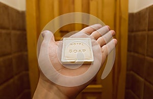 Inside the hotel room, one hand of a visitor holding small piece of bathe soap frjm toiletries in a guest house bathroom photo