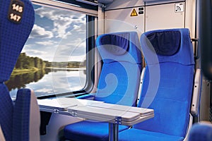 Inside of modern express train. Nobody in blue chairs at window. Comfortable chairs and table in foreground, nature outside window