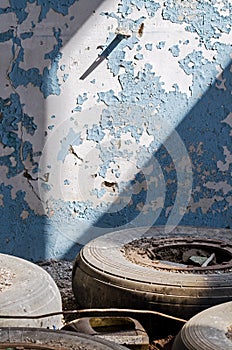 Inside An Old Abandoned Industrial Building, Factory. The Wall With Peeling Blue Paint. Used Tires, Wheels. Many Different Garbage