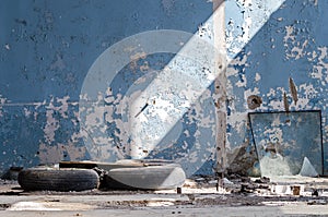 Inside An Old Abandoned Industrial Building, Factory. The Wall With Peeling Blue Paint. Used Tires, Wheels. Many Different Garbage