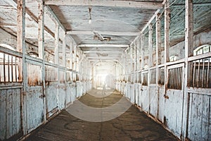 Inside old wooden stable or barn with horse boxes, tunnel or corridor view with light in the end