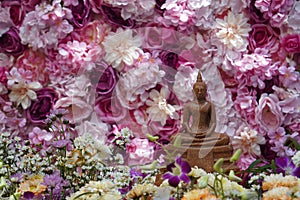 inside right, front view brown buddha in front of blur various flowers, blur wall flowers and roses colorful background, worship,