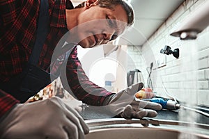 Inside view. Close-up of handsome plumber repairing sink in kitchen