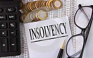 INSOLVENCY - word on a white piece of paper on the background of a calculator, pennies and glasses